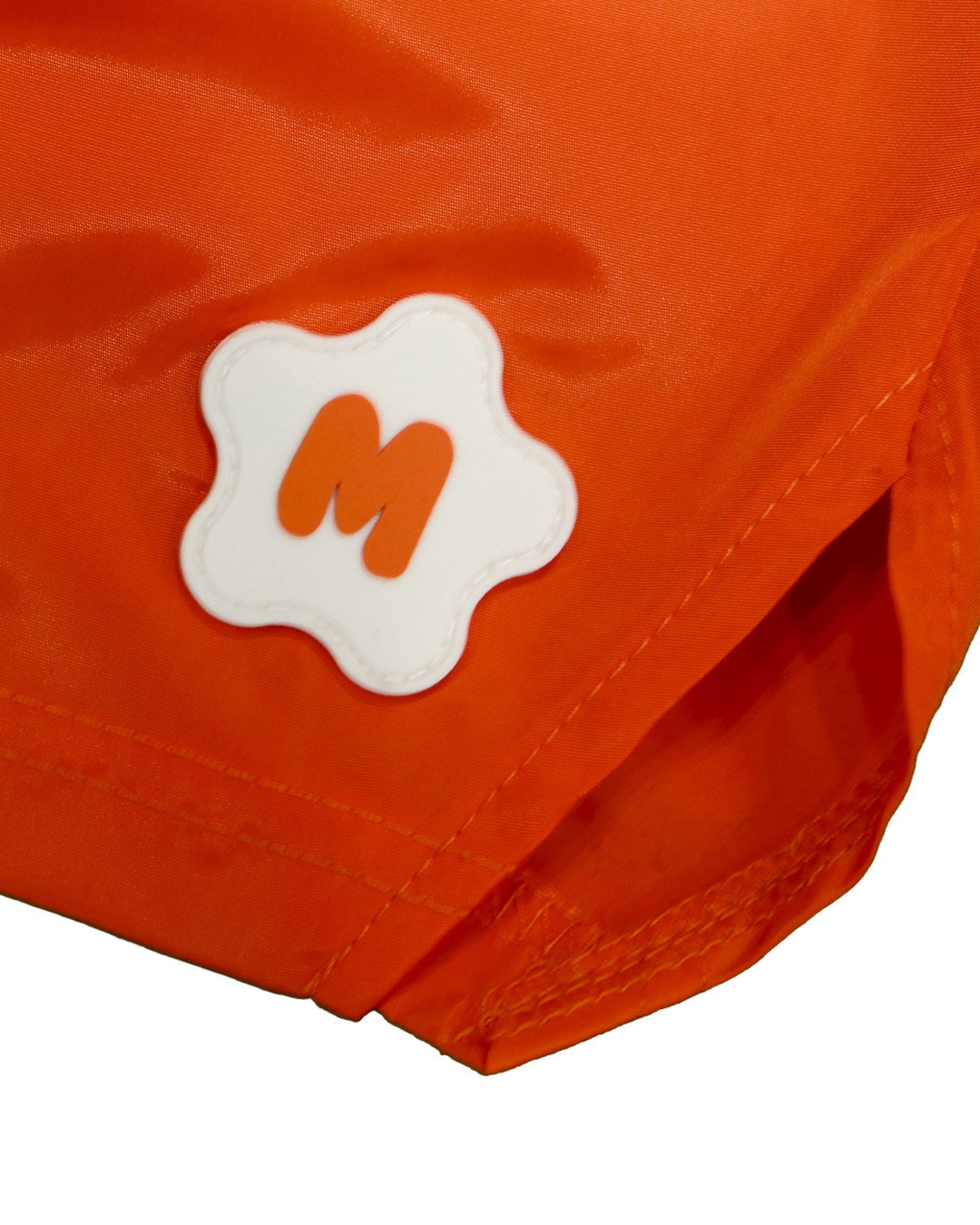 Orange nylon shorts with rubber logo detail on the left leg.